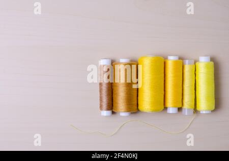 Flache Spulen mit bunten gelben und braunen Fäden, die auf einem Holztisch oder Tisch in Reihe angeordnet sind, Heimarbeit, drinnen, Nähset, Nahaufnahme Stockfoto