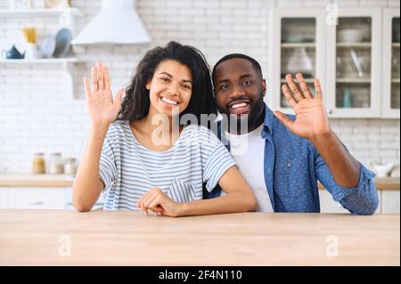 Videochat mit einem afroamerikanischen Paar, fröhlicher Birazialfrau und Mann, die auf die Kamera schauen und Hallo. winken Virtuelles Treffen mit Familie oder Freunden, Videoanruf während Pandemie, Webcam-Ansicht Stockfoto