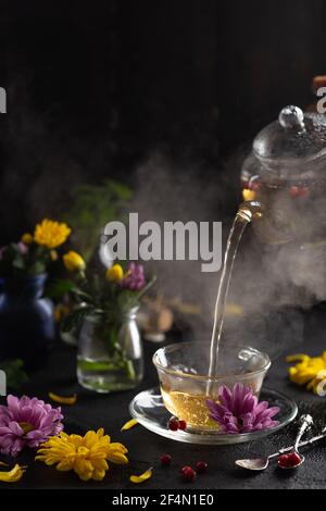 Prozess Brühtee, dunkle Stimmung. Der Dampf aus heißem Tee wird aus dem Wasserkocher gegossen. Blumen. Warmes Essen und gesundes Essen Konzept Stockfoto