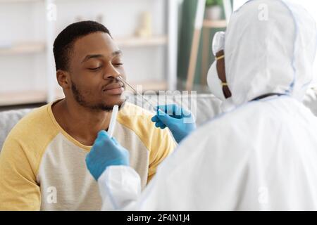 Arzt in PSA-Anzug nimmt Tupfer zum Patienten zu Hause Stockfoto