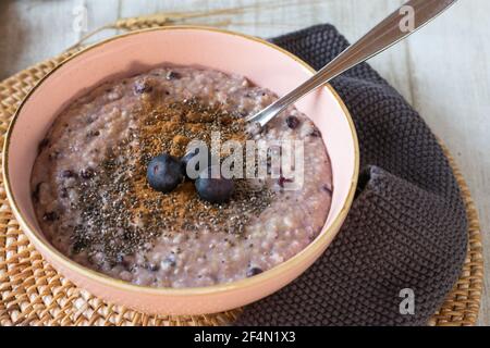 Gesundes Frühstücksbrei mit Heidelbeeren, Chiasamen und Zimt warm in einer Schüssel von oben serviert. Isolierte und Nahaufnahme Stockfoto