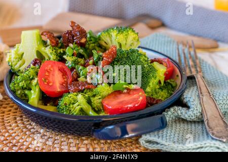 Brokkoli-Salat mit frischen und getrockneten Tomaten, Knoblauch, in Balsamico-Essig marinierten roten Zwiebeln und Olivenöl-Dressing in einer Schüssel serviert Stockfoto
