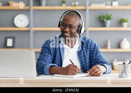 E-Education. Happy schwarz reifen Mann mit Laptop und Notizen, Hören Online-Kurs Stockfoto