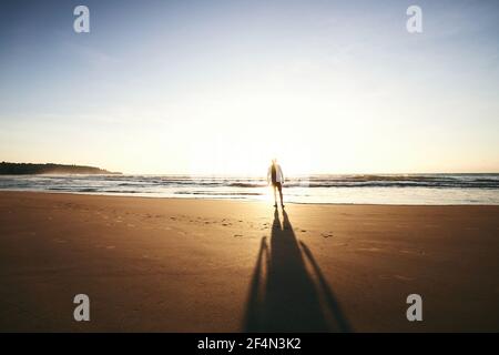 Silhouette einer einsamen Person am leeren Strand. Rückansicht des Menschen während des Sonnenaufgangs. Sandige Küste von Sri lanka. Stockfoto