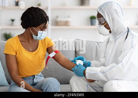 Krankenschwester im Schutzanzug, die Blutprobe für weibliche Patienten nimmt Stockfoto