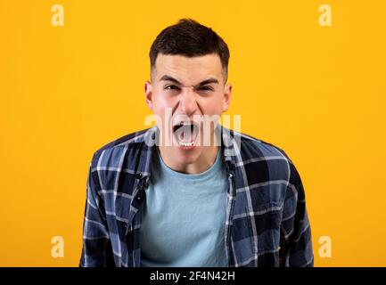 Frustrierter junger Mann, der vor Wut schreit und seine Wut über orangen Studiohintergrund ausdrückt. Konzept der negativen Emotionen Stockfoto