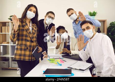 Happy Creative Office Worker Team in Gesichtsmaske winkt Hallo Zum Kamerahochformat Stockfoto