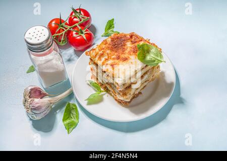 Mediterrane Küche, traditionelle italienische Lasagne Pasta, mit Bolognese, Bechamel und Käse. Auf trendigem breiht hellblauem Hintergrund mit hartem Licht und Stockfoto