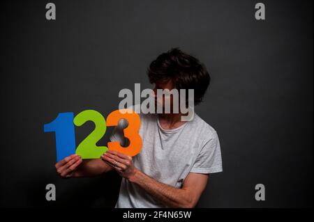 Ein junger Mann in einem weißen T-Shirt mit bunten Schaumstoffnummern 1, 2 und 3. Stockfoto