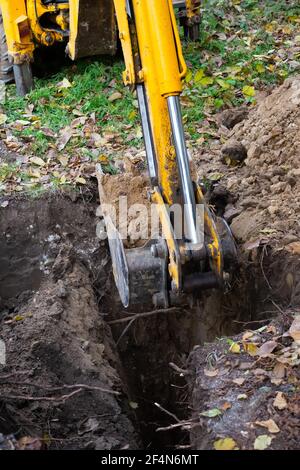 Der Bagger schaufelt Erde mit Ton aus der Grube mit einem Eimer für den Bau eines Klärgruben. Bodenarbeiten der Maschine. Stockfoto