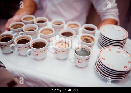 Selektiver Fokus eines Mannes, der ein Tablett mit Tassen hält Voller Kaffee und Untertassen Stockfoto