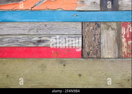 Verblasste orange, rote und blaue Farbe auf grau verwittertem Holz Stockfoto