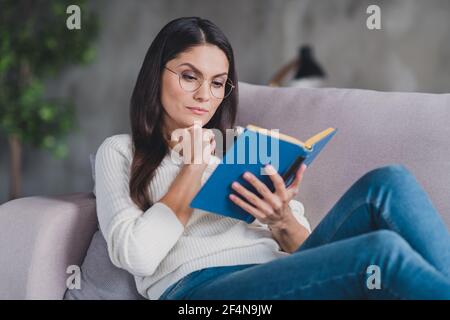 Foto von gesinnten ernst Mädchen lag Couch Rest lesen Lehrbuch Tragen Sie Brillen weißen Pullover im Wohnzimmer zu Hause drinnen Stockfoto