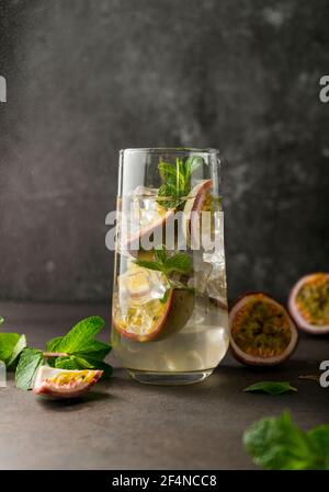 Erfrischendes Getränk mit Passionsfrucht. Cocktail mit tropischen Früchten auf dunklem Hintergrund. Mit grünen Minzblättern. Vertikale Position Stockfoto