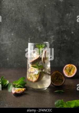 Erfrischendes Getränk mit Passionsfrucht. Cocktail mit tropischen Früchten auf dunklem Hintergrund. Mit grünen Minzblättern. Vertikale Position Stockfoto