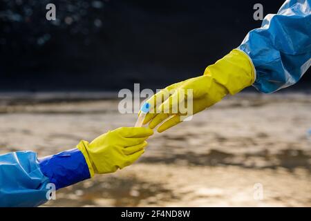 Handschuhen von Ökologen in schützenden Overalls unter Kolben mit Probe von giftigem Wasser aus dem von ihrem Kollegen gegen Verschmutzter Fluss Stockfoto
