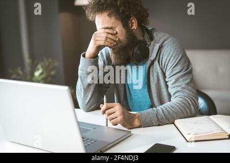 Facepalm. Krise in der Wirtschaft. Ein trauriger Mann sitzt am Arbeitsplatz und bedeckt sein Gesicht mit der Hand. Stockfoto