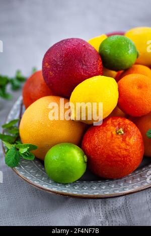 Frische saftige Zitrusfrüchte - Orangen, Mandarinen, Zitronen und Limetten, auf grauem Hintergrund Stockfoto