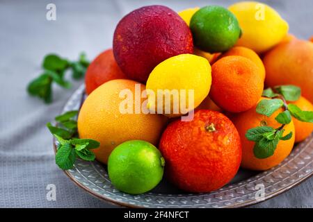 Frische saftige Zitrusfrüchte - Orangen, Mandarinen, Zitronen und Limetten, auf grauem Hintergrund Stockfoto