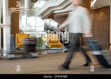 Verschwommene Bewegung der modernen Geschäftsmann zieht Koffer hinter sich, während Umzug entlang der Halle des großen und luxuriösen Hotel Stockfoto