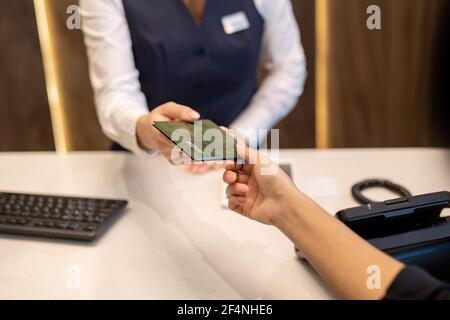 Hand der jungen weiblichen Rezeptionistin, die den Pass an einen der übergibt Neue Gäste des Hotels über Rezeptionsschalter mit Telefon und Tastatur Stockfoto