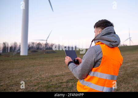 Elektroingenieur überprüft oder repariert Windenergieanlagen im Feld mit einem Tablet. Stockfoto