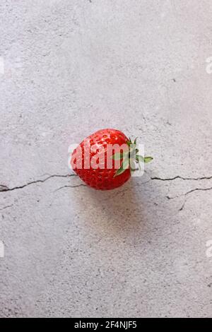 Erdbeere mit Grünpflanzen liegt auf einem steingrauen Tisch. Stockfoto