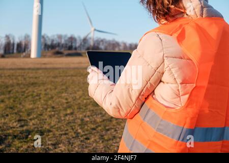 Eine Ingenieurin überprüft oder repariert Windmühlen oder Windenergieanlagen mit einem Tablet in einem orangefarbenen vesta. Stockfoto