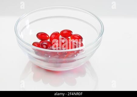 Krillöl-Kapseln. Rote Gelatinekapseln mit Krillöl in einer transparenten Glasschale auf weißem Hintergrund.Quelle von Omega-Fettsäuren.Diät Stockfoto