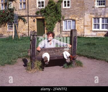 Junger Mann posiert in Dorfbeständen, Market Square, Stow-on-the-Wold, Gloucestershire, England, Vereinigtes Königreich Stockfoto