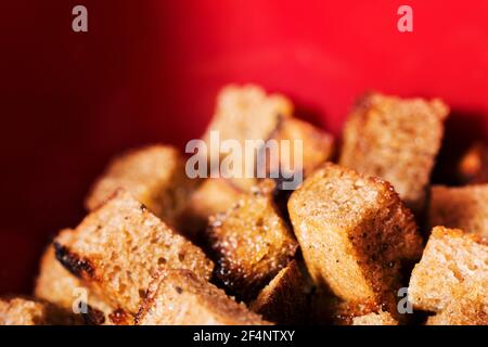 Croutons aus schwarzem Brot auf rotem Hintergrund. Leckere knusprige knusprige Cracker. Bild mit geringer Schärfentiefe Stockfoto