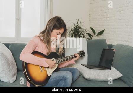 Attraktive Musikerin Frau spielt E-Gitarre während Online-Konzert zu Hause in Isolation. Musiklehrer Unterricht spielen Instrument online mit l Stockfoto