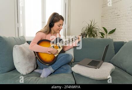 Attraktive Musikerin Frau spielt E-Gitarre während Online-Konzert zu Hause in Isolation. Musiklehrer Unterricht spielen Instrument online mit l Stockfoto