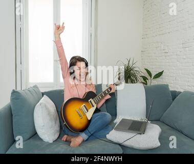 Attraktive Musikerin Frau spielt E-Gitarre während Online-Konzert zu Hause in Isolation. Musiklehrer Unterricht spielen Instrument online mit l Stockfoto