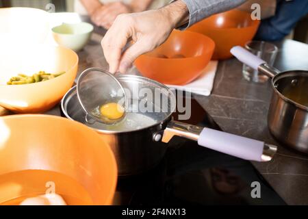 Hand eines älteren Mannes, der Eigelb aus rohem Ei in die Hand nimmt Sieben Sie aus der Metallpfanne, die auf dem Tisch steht, während Sie etwas kochen Im Meisterkurs in der Küche Stockfoto