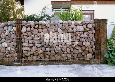 Eine spezielle Form eines Gabions aus Kieselsteinen. Selbstgemachter Zaun aus Steinen. Stockfoto