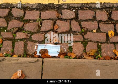Nasse medizinische Maske fiel auf die Straße, pandemischer, nicht nachhaltiger Müll, der auf dem Bürgersteig zurückgelassen wurde. Schmutzige Gesichtsbedeckung, die in Oxford kargelhaft auf den Boden gelegt wird Stockfoto