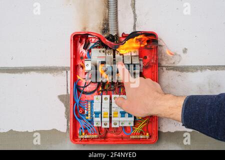 Männliche Hand schaltet brennende Schalttafel von Überlast oder Kurzschluss ab Schaltkreis an der Wand Stockfoto