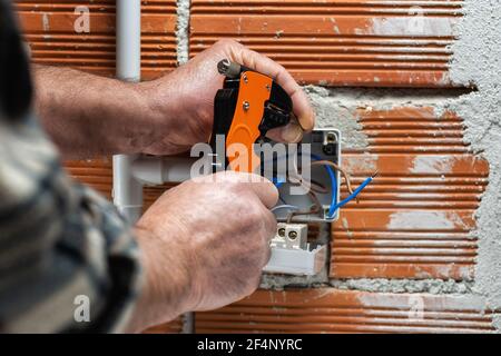 Elektriker Arbeiter bei der Arbeit mit Abisolierer bereitet die elektrischen Kabel der häuslichen elektrischen Anlage. Bauindustrie. Stockfoto