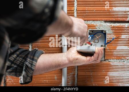 Elektriker Arbeiter bei der Arbeit mit einem Schraubendreher fixiert das Kabel in der Klemme des Schalters einer Wohnelektrik. Bauindustrie. Stockfoto