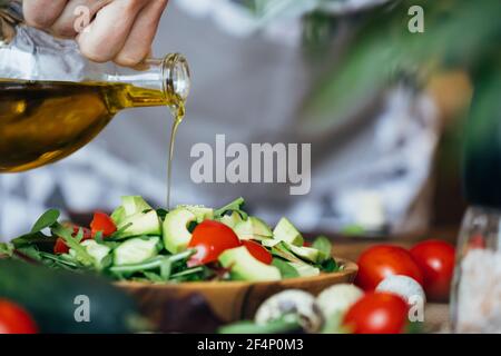 Olivenöl mit Tomaten, Avocado und Gurke von Hand auf den Salat gießen. Stockfoto