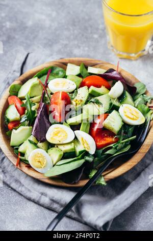 Grüner Salat mit Tomaten, Avocado, Gurken und Eiern auf Holzplatte und Orangensaft auf dem Tisch. Stockfoto