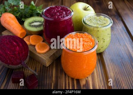 Verschiedene Gemüse- und Obstsmoothies oder Püree in den kleinen Gläsern auf dem braunen Holzhintergrund. Nahaufnahme. Stockfoto