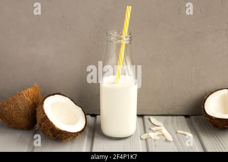 Kokosmilch in der Glasflasche und Kokosnüsse auf der Grauer Hintergrund Stockfoto