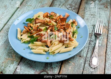 Italienische Penne Pasta mit Waldpfifferlingen mit Jahrgangsgabel Auf einem alten, schäbigen, türkisfarbenen Tisch aus der Nähe Stockfoto