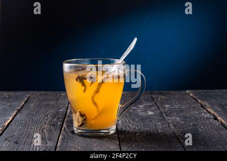Durchsichtiger Becher aus Glas mit Tee. Teeblätter in einem Becher. Tee in einer Tasse zubereiten. Einen Teelöffel in einem Becher. Vorderansicht. Stockfoto