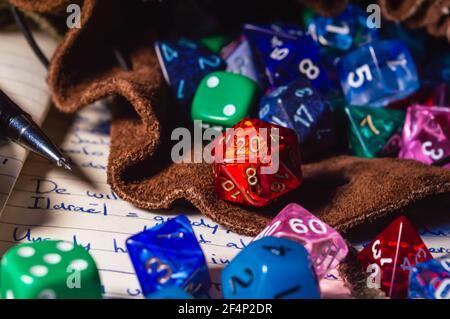 Nahaufnahme eines Rollenspiels Würfel verschiedener Formen und Farben, die aus einer Lederwürfeltasche auf einem offenen Notizbuch auslaufen. Stockfoto