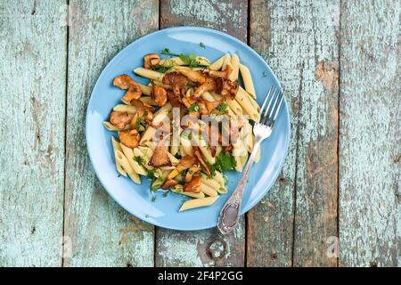 Vegane Penne Pasta mit Waldpfifferlingen in türkisfarbenem Teller Auf altem hölzernen Tisch copyspace oben Ansicht Stockfoto