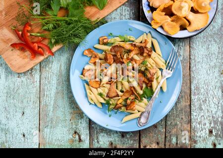 Veganes Gericht von Penne Pasta mit gebratenen Waldpfifferlingen Pilze In türkisfarbenem Teller mit frischen Pilzen und Gemüse oben Stockfoto