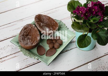 Zwei Hälften Schokolade Osterei, auf einem kleinen alten Tablett neben Mini-Schokolade und Blumen. Stockfoto